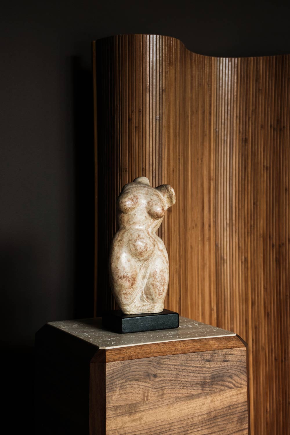 antique stone woman sculpture on wooden pedestal in moody modern interior design